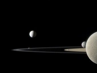 Энцелад (в центре), Рэя (половинка справа крупным планом) и Мимас (выглядывает из-за Рэи) на фоне колец спутника. Фото NASA/JPL/SSI/Jason Major.